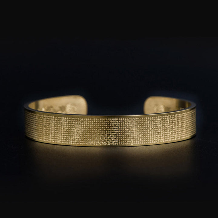 Goldenes Armband mit feiner Gravierung auf schwarzem Hintergrund elegant.