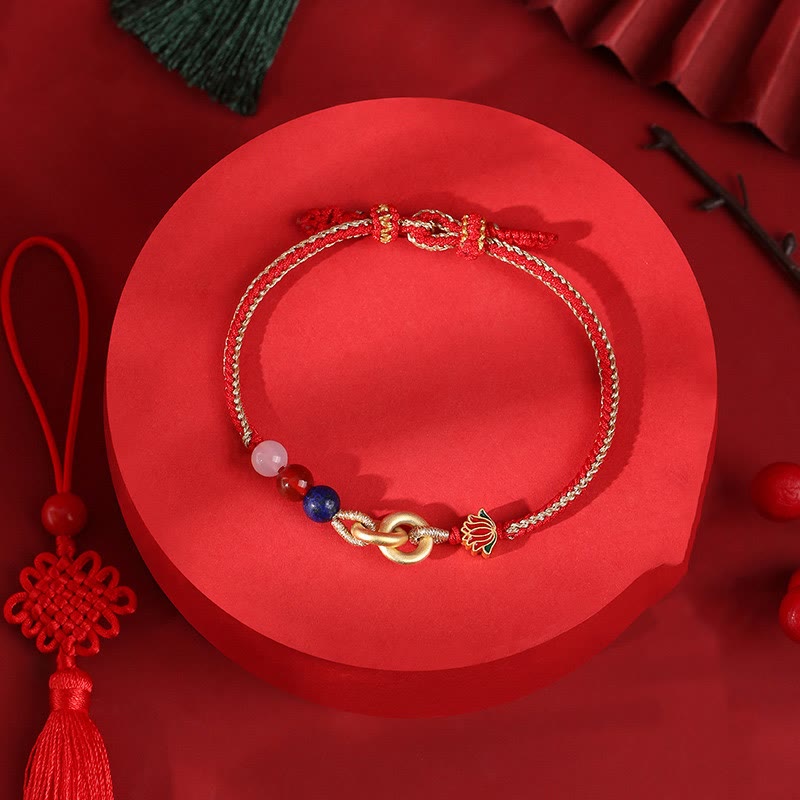 Goldenes Armband mit Lotus-Anhänger und bunten Perlen auf rotem Untergrund.