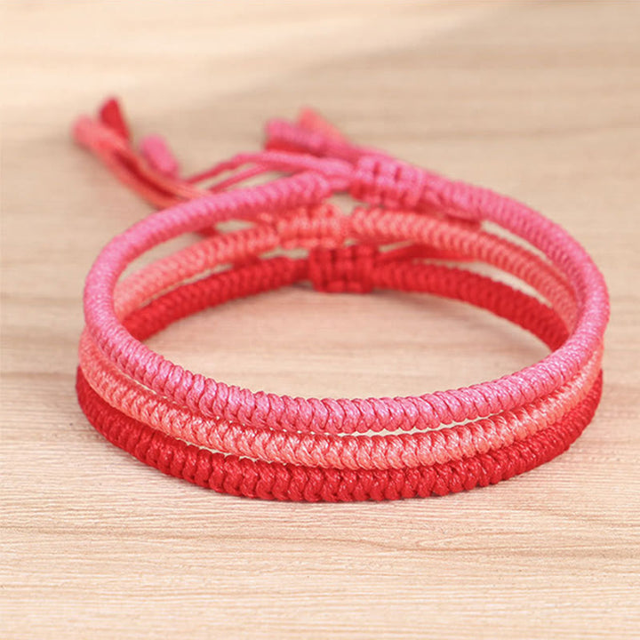 Tibetisches geflochtenes Armband in Rosa und Rot auf Holz.