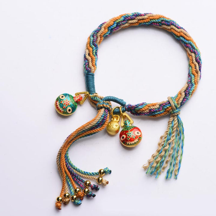 Buntes Seil-Armband mit goldenen Glöckchen und Perlen auf weißem Hintergrund.