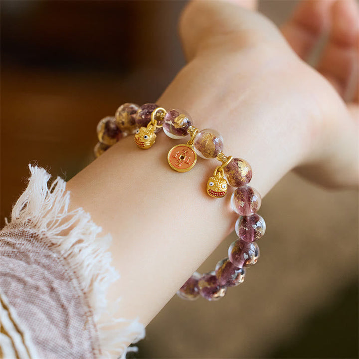 Armband mit lila Perlen und goldenen Charms am Handgelenk getragen.