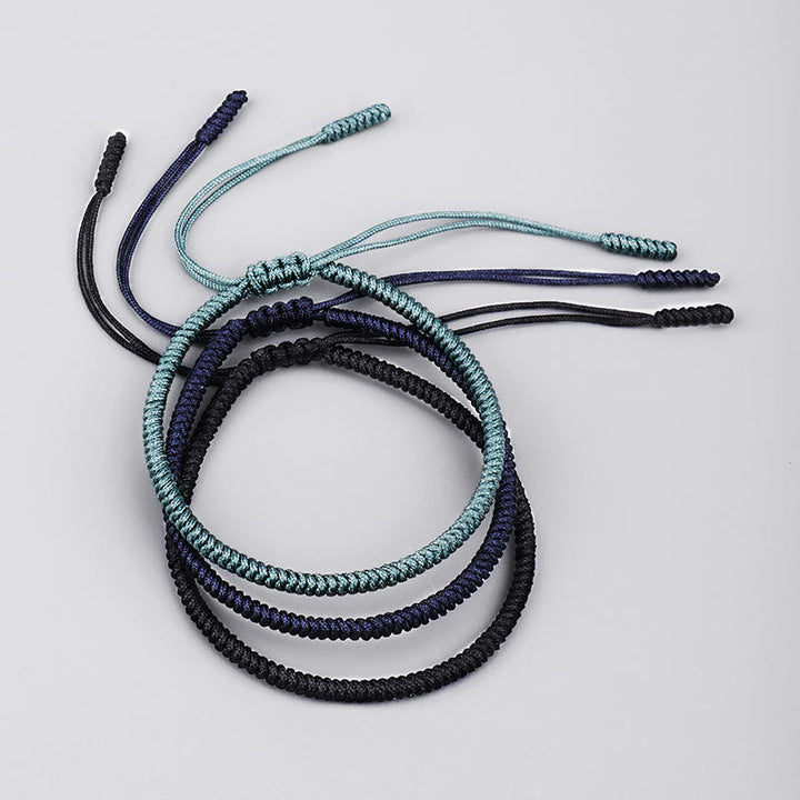 Drei geflochtene Armbänder in Schwarz, Dunkelblau und Hellblau nebeneinander.