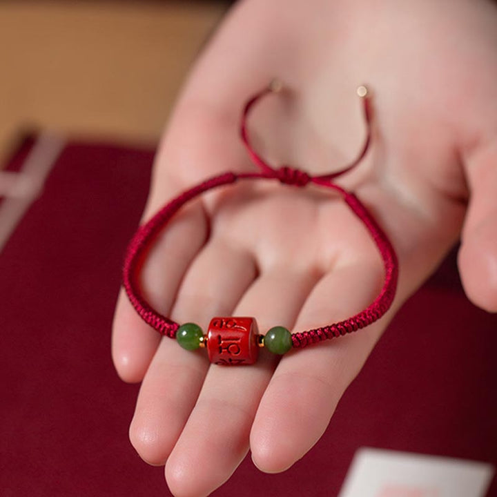 Rotes Armband mit Om Symbol und grünen Jadekugeln am Handgelenk.
