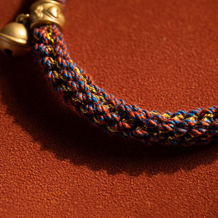 Buntes geflochtenes Armband mit goldenem Verschluss auf rotem Hintergrund.