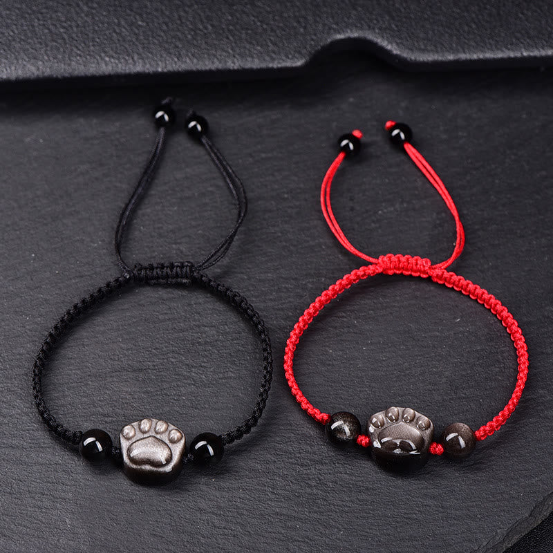 Zwei Armbänder mit Pfotenmotiv in Schwarz und Rot auf Stein.