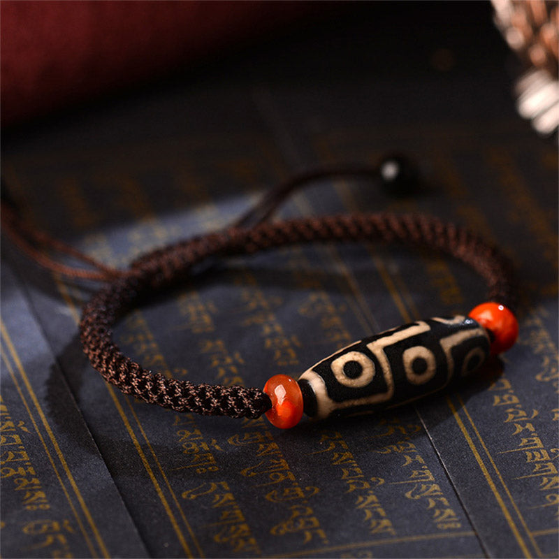 Dzi-Perle Neun Augen Armband mit roten Achatsteinen auf Buch, braunes Geflecht
