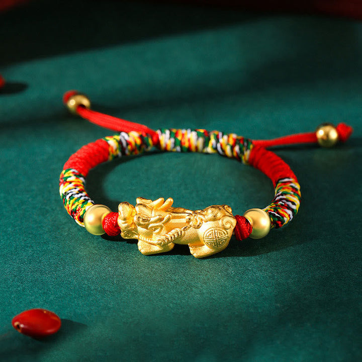 Goldenes Pixiu Armband mit roten Perlen auf grünem Hintergrund.