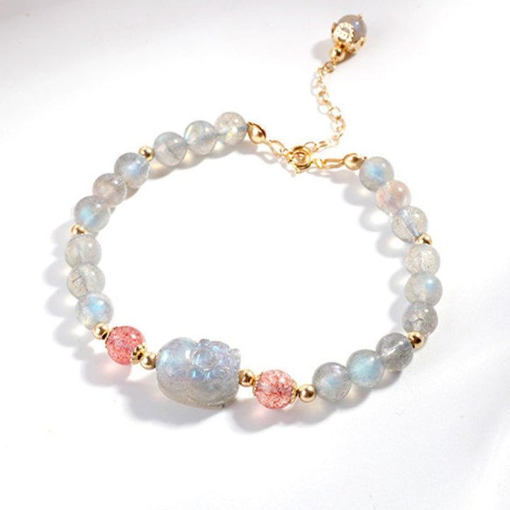 Armband mit Erdbeerquarz, Mondstein und goldfarbenen Perlen auf weißem Hintergrund.