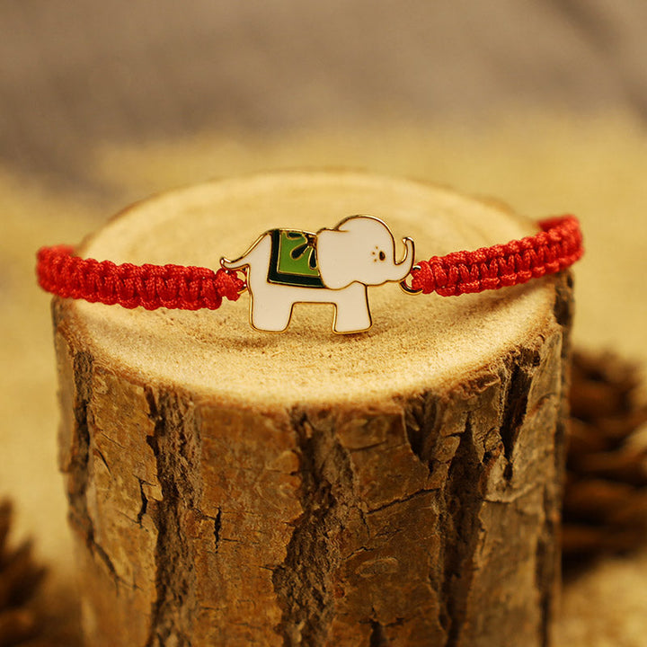 Rotes Armband mit Elefant Charm auf Holzstamm Nahaufnahme.