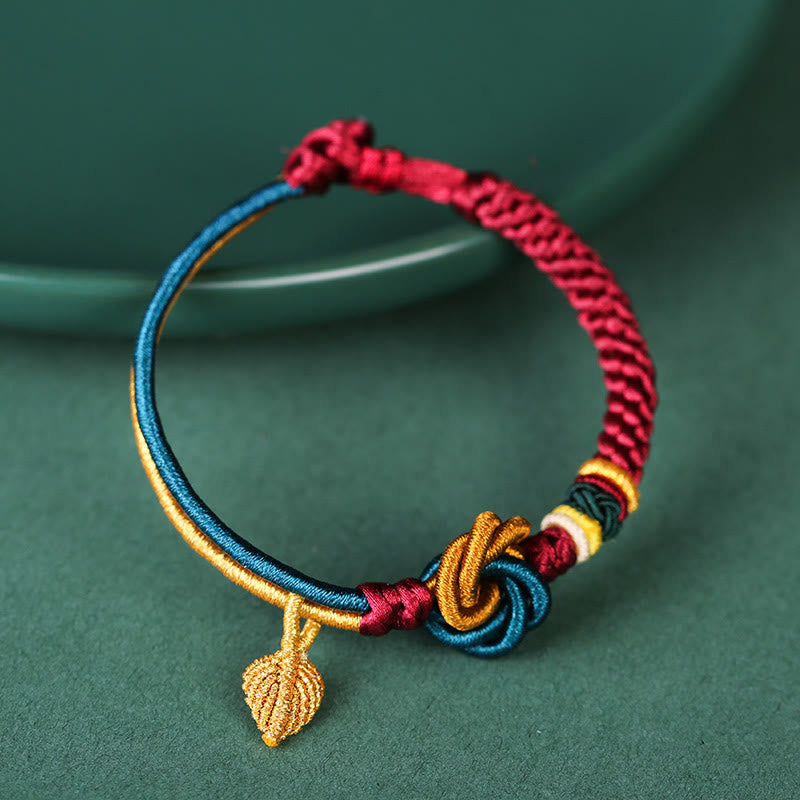 Tibetisches Armband buntem Seidenfaden Blattanhänger grünem Hintergrund Nahaufnahme