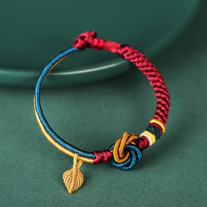 Tibetisches Armband buntem Seidenfaden Blattanhänger grünem Hintergrund Nahaufnahme