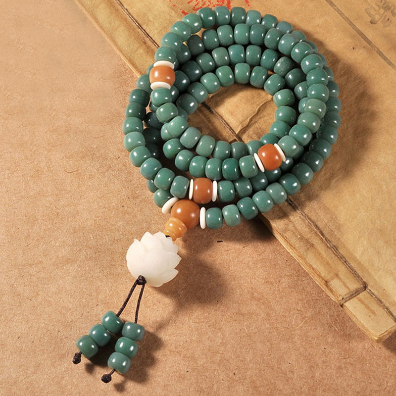Grünes Bodhi Lotus Armband mit Erfolgssymbolen auf Holzuntergrund.