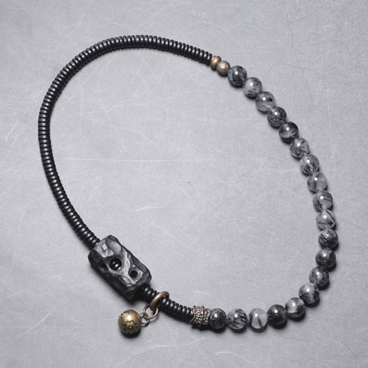Armband mit schwarzen Perlen und metallischen Akzenten auf grauem Hintergrund.