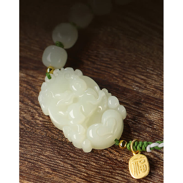 Weißes Jade Armband mit Glücksmünze auf Holzoberfläche.