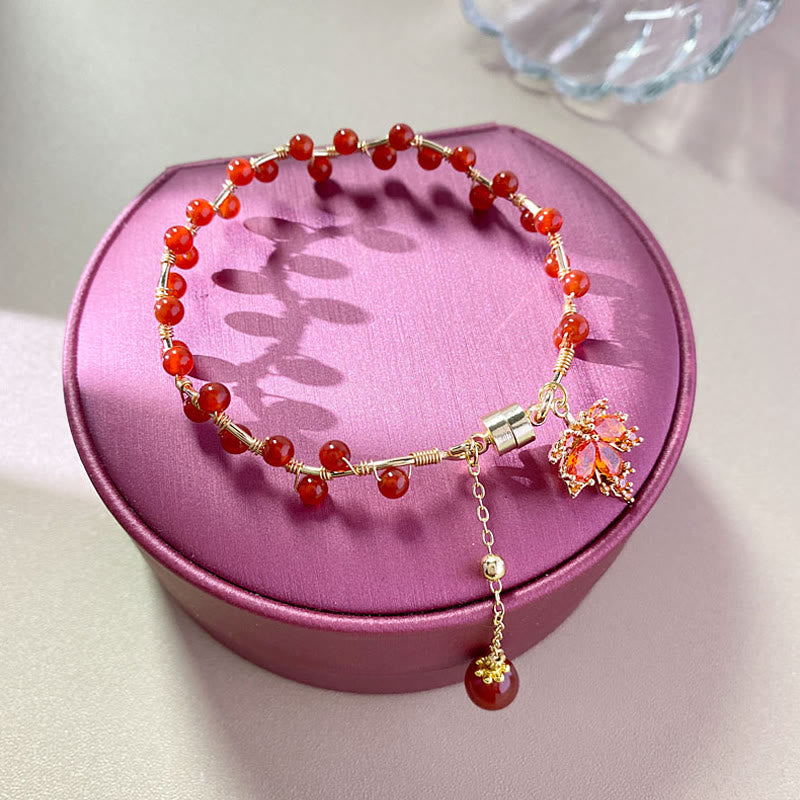 Rotes Armband mit Ahornblatt Charm auf rosa Schmuckbox präsentiert.