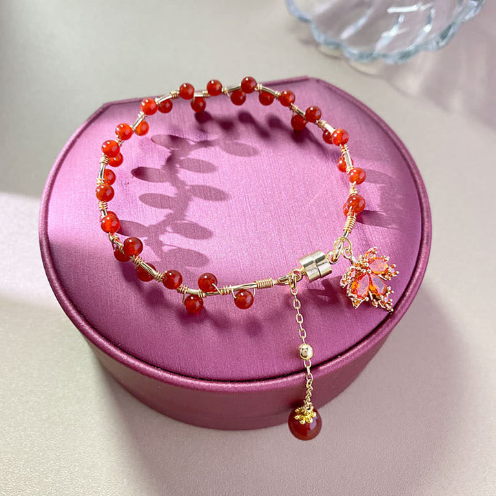 Rotes Armband mit Ahornblatt Charm auf rosa Schmuckbox präsentiert.