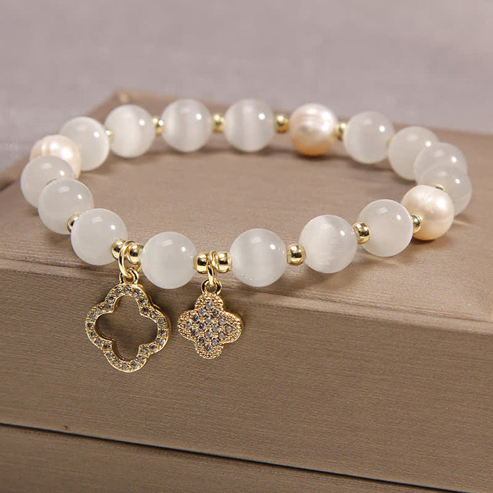 Weißes Perlen Armband mit goldenen Vier-Blatt Anhängern auf Holz.