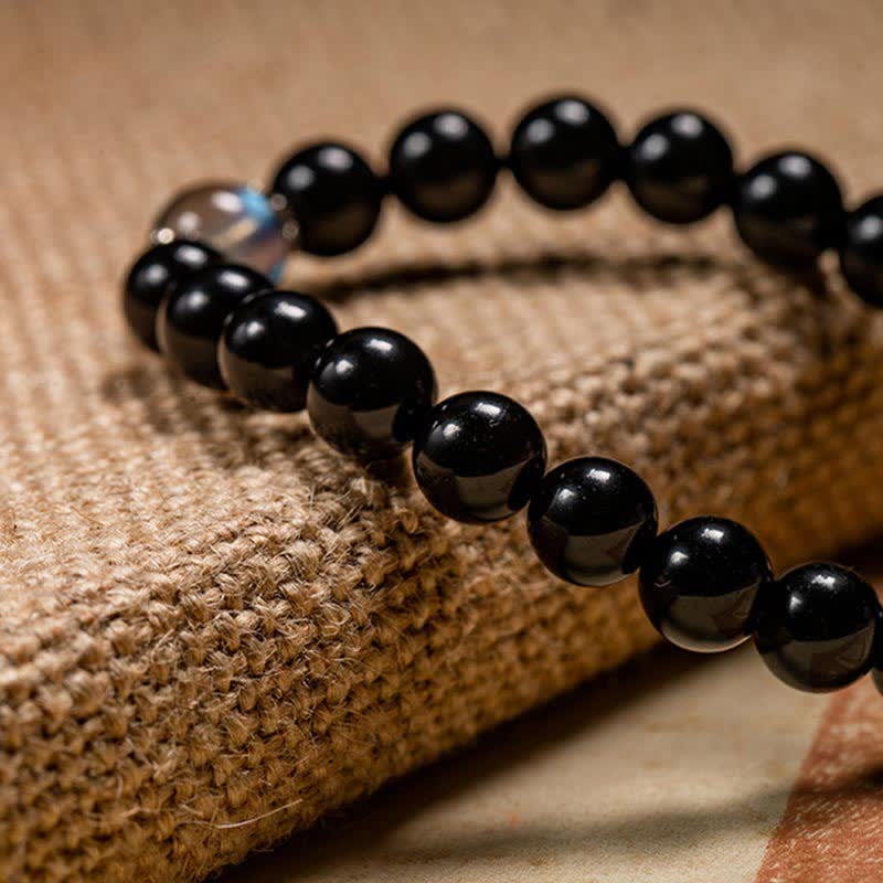 Schwarzes Obsidian Armband mit glänzenden Perlen auf Naturstoff draped.