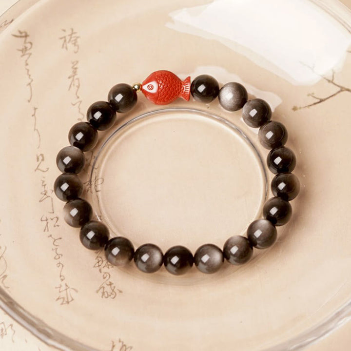 Obsidian Armband mit rotem Koi Fisch Charm auf cremefarbenem Hintergrund