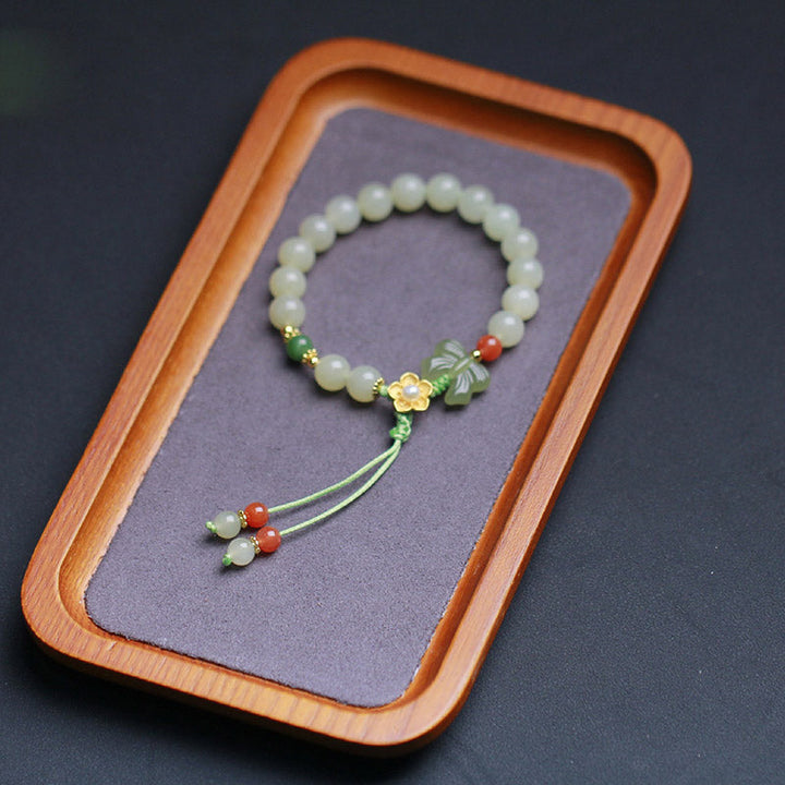Jadegrünes Armband mit Perlen, Blüte und Schmetterling Anhänger elegant präsentiert.