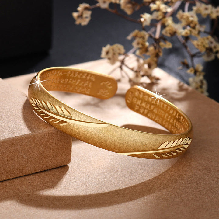 Goldenes Armband mit Feder-Design auf beiger Oberfläche elegant.