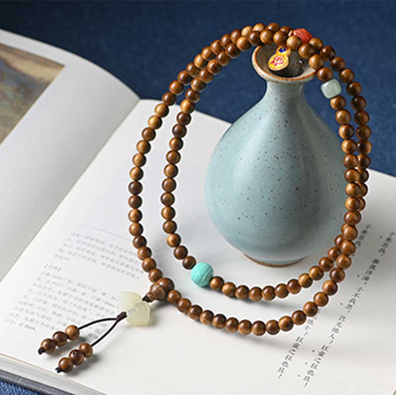 Mala Rosenholz Perlenarmband mit türkiser Verzierung auf Buch.