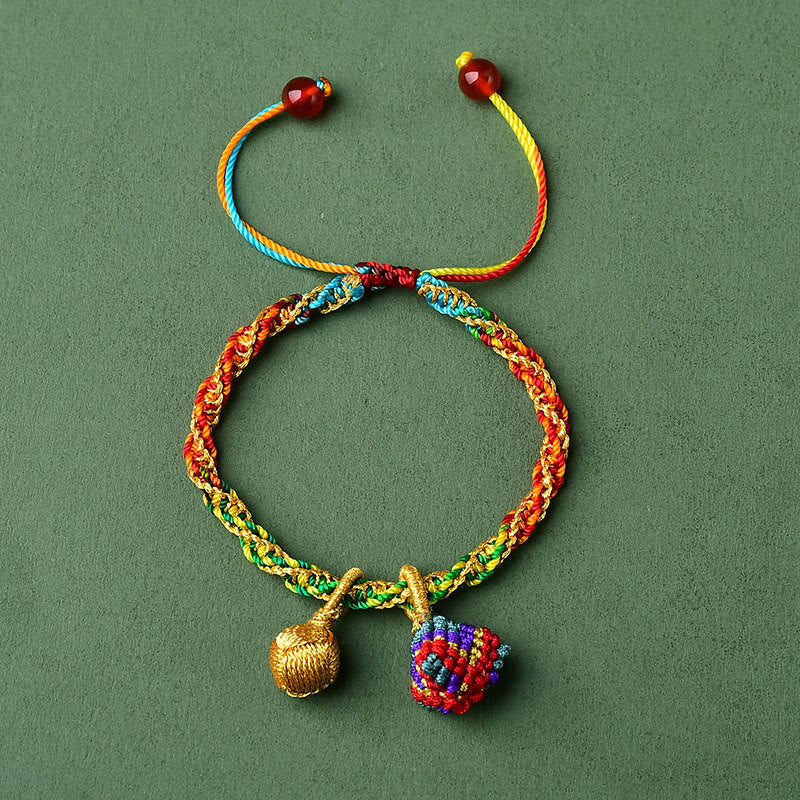 Buntes Armband mit goldener Glocke und Zongzi Anhänger auf grünem Hintergrund.