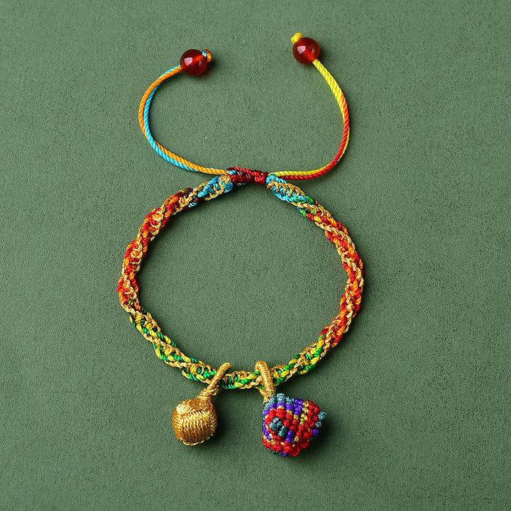 Buntes Armband mit goldener Glocke und Zongzi Anhänger auf grünem Hintergrund.