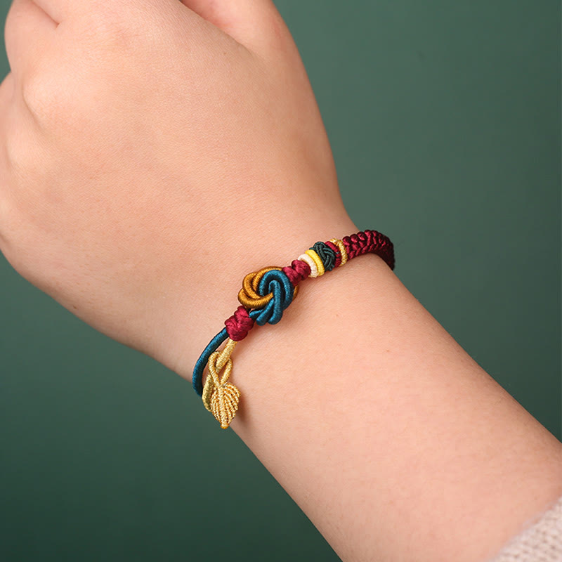 Tibetisches Armband am Handgelenk mit bunten Knoten und goldenem Blatt Glücksbringer