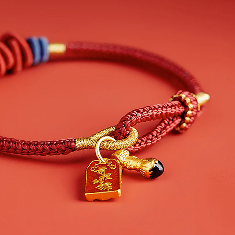 Rotes Seidenarmband mit goldenem Anhänger auf rotem Hintergrund elegant.