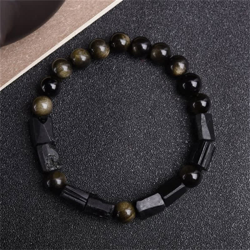 Obsidian Armband mit goldenen Perlen auf schwarzem Stoff, Wohlstand.