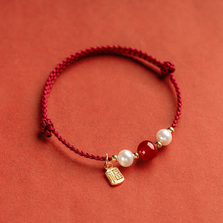 Rotes Armband mit Perlen und Fu-Zeichen Charm auf korallenfarbenem Hintergrund.
