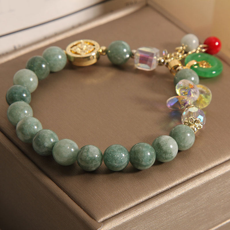 Grünes Jade Armband mit Glückszeichen Charmen auf beigem Untergrund.