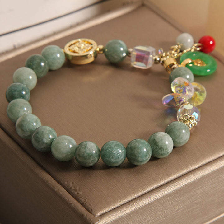 Grünes Jade Armband mit Glückszeichen Charmen auf beigem Untergrund.