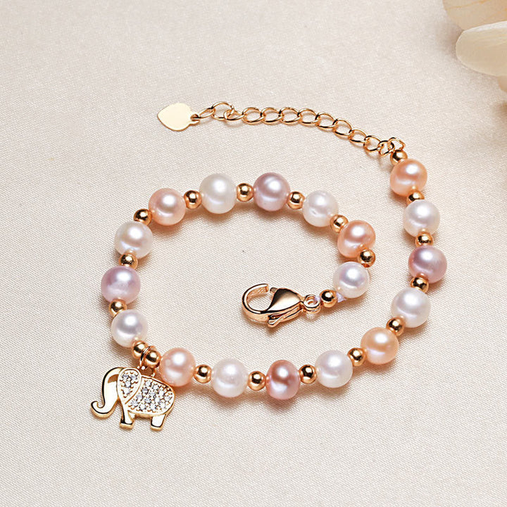 Armband Perle Elefant rosegold mit weißen und rosa Perlen auf Leinenhintergrund.