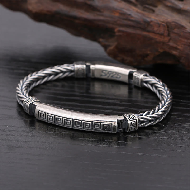 Silbernes Armband mit Flechtmuster und graviertem Muster auf Holz.