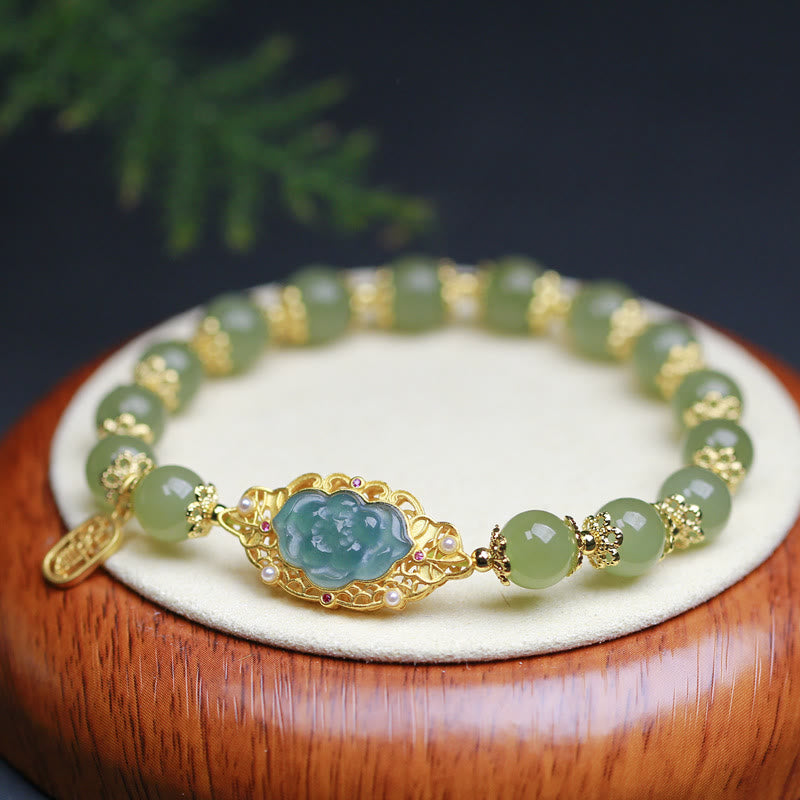 Jade-Armband mit Lotus-Anhänger goldfarben elegant auf weißem Tablett.