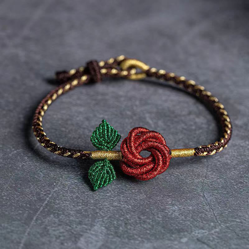 Bestickertes Armband mit roter Blüte und grünen Blättern auf grauem Hintergrund