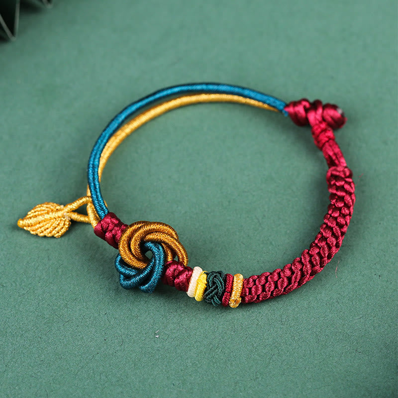 Tibetisches Armband mit bunten Knoten, Blatt und Glückssymbolen auf grünem Hintergrund.