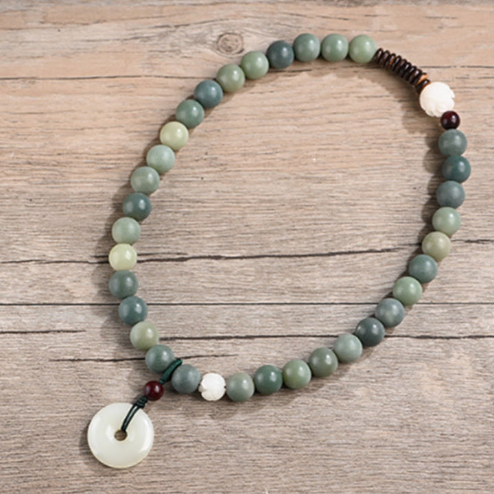 Jade Lotus Armband mit weißem Anhänger auf Holzuntergrund
