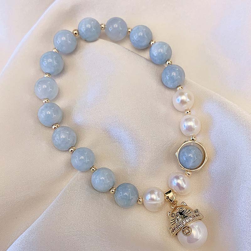 Armband Aquamarin Perle Katze – Glück & Heilung auf Creme Stoff präsentiert