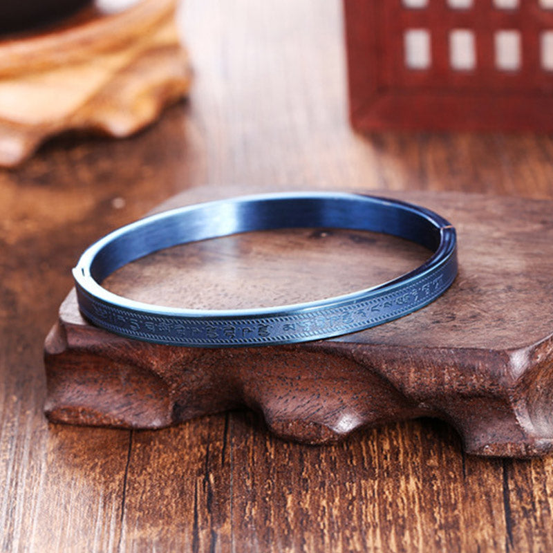Blaugraues Titanstahl Armband mit Segenmuster auf Holzoberfläche.