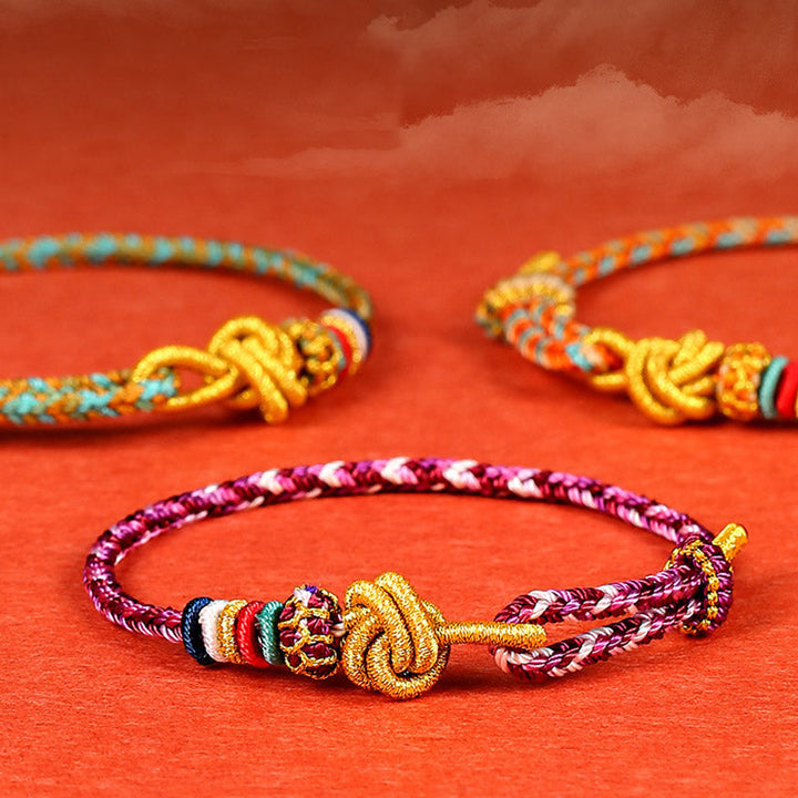 Bunte geflochtene Armbänder mit goldenen Verschlüssen auf rotem Hintergrund.