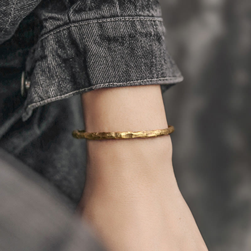 Goldenes strukturiertes Armband am Handgelenk mit grauer Jeansjacke getragen