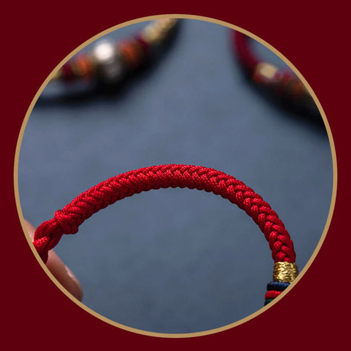 Rotes geflochtenes Armband mit goldener Verschlussdetail am Handgelenk getragen.