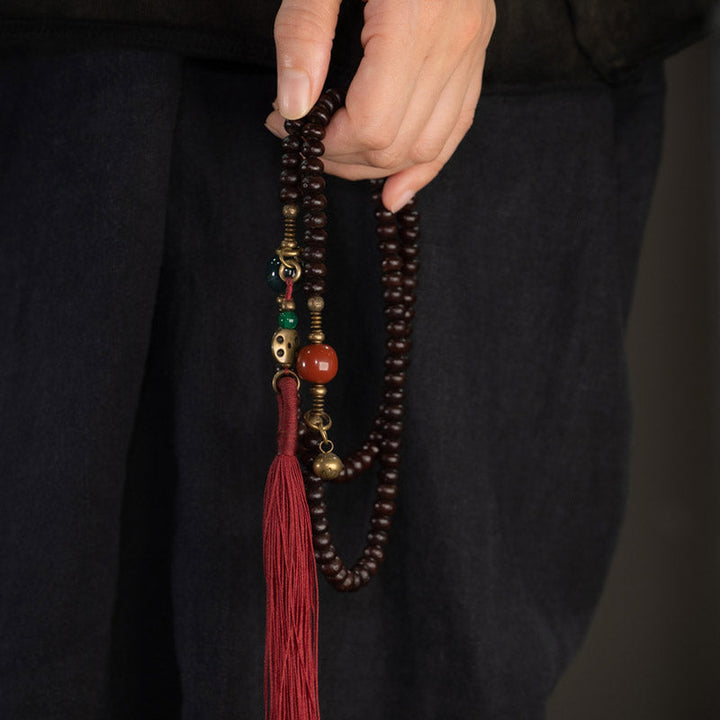 Mala 108 Perlen Bodhi – Stärke Armband mit roter Quaste wird gehalten.