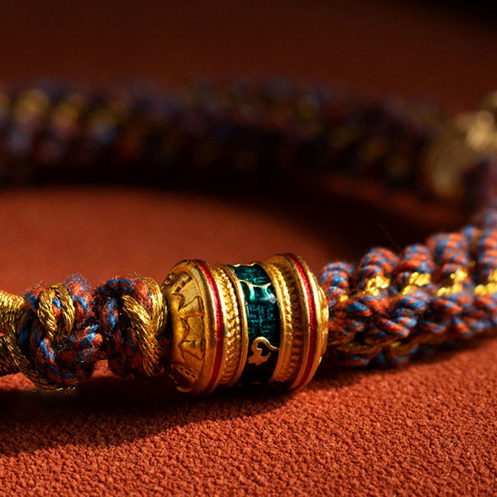Buntes Armband mit goldenen Ringen auf terrakottafarbenem Untergrund.