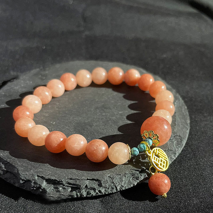 Pfirsichfarbenes Perlenarmband mit goldenen Türkis-Anhängern auf Stein.