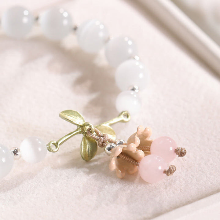 Armband mit Rosenquarz und Perlmuttblüte auf beigem Stoff.
