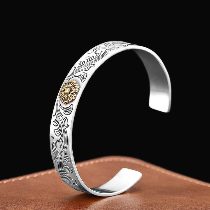 Silbernes Armband mit Blumenmotiv und Goldakzenten auf Braun.